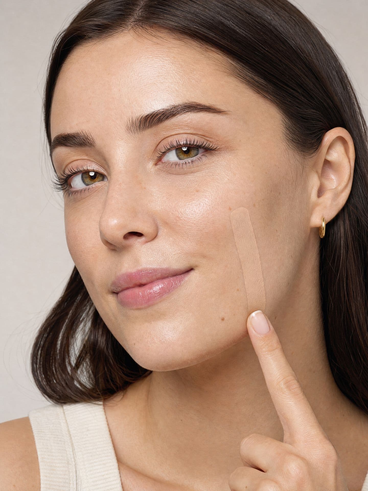 A woman pointing at a foundation swatch drawn along her cheek.